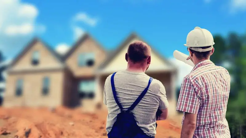Deux ouvriers du bâtiment debout devant une maison.