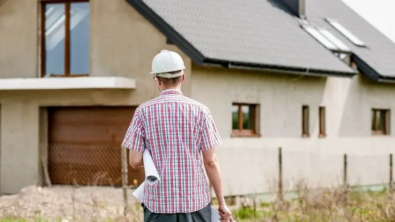Un homme portant un casque de chantier devant une maison.