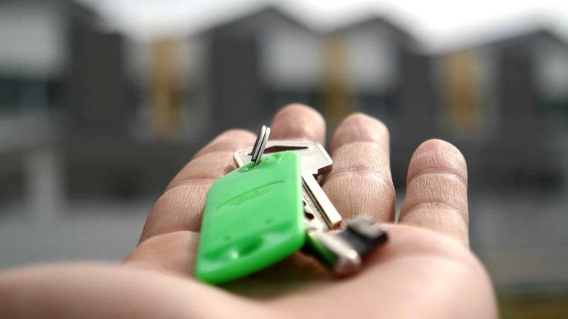 Une personne tenant une clé verte avec une maison en arrière-plan.