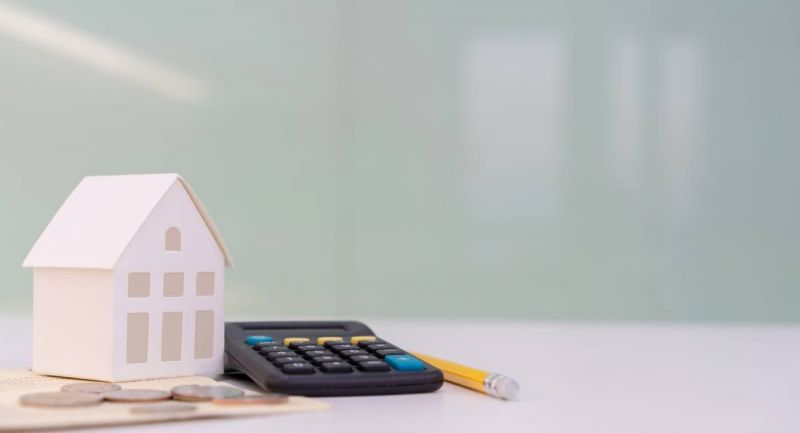 Un modèle de maison sur une table à côté d'une calculatrice et d'argent.