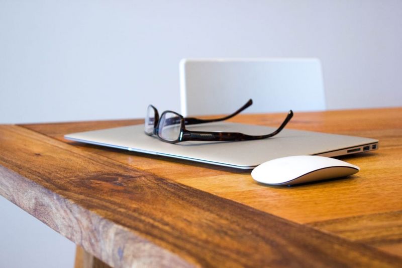Un ordinateur portable sur un bureau en bois avec des lunettes et une souris.