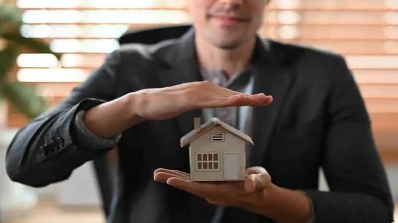 Home insurance concept. Young man hand protecting holding model.