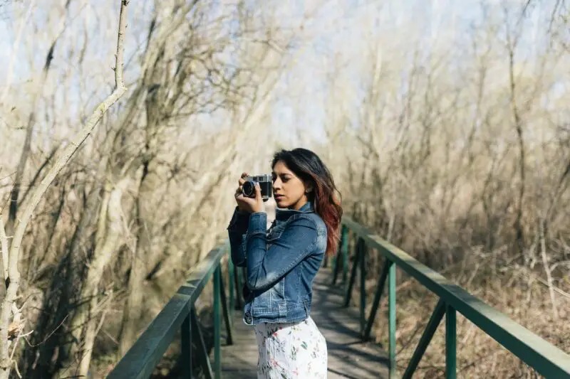 Une femme prenant une photo avec son appareil photo sur un pont dans les bois