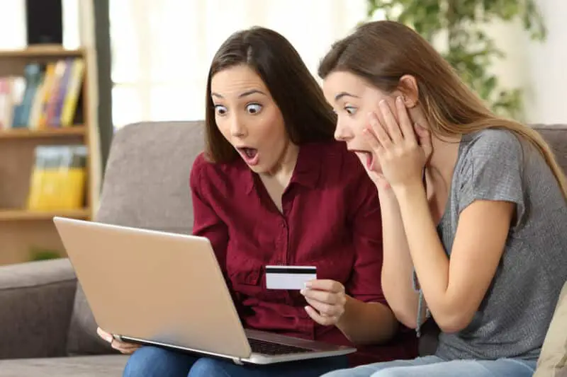 Deux femmes assises sur un canapé avec un ordinateur portable et une carte de crédit.
