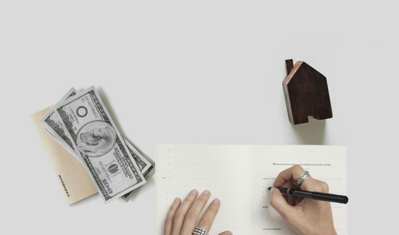 La main d une femme écrivant sur un carnet à côté de l argent et d une maison
