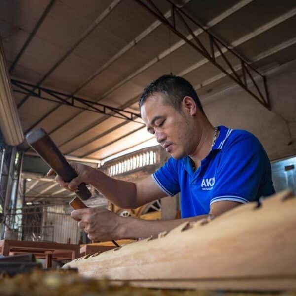 Un homme en chemise bleue travaille sur un instrument en bois.