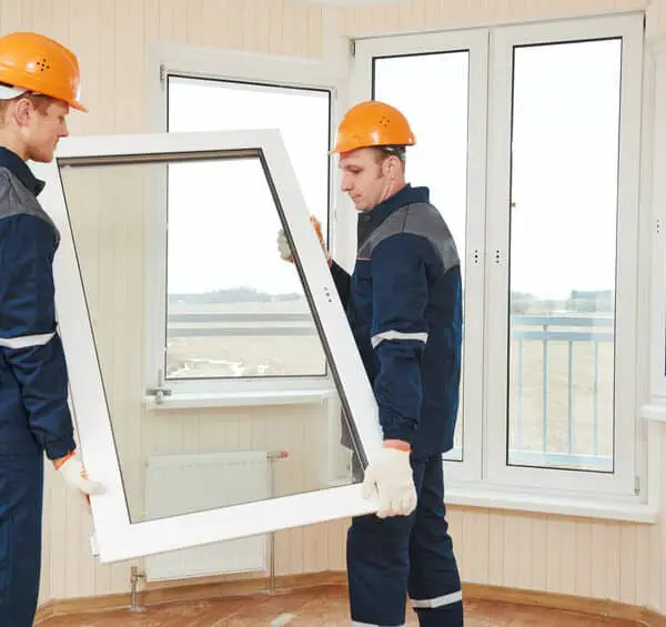 Deux ouvriers du bâtiment installent une fenêtre dans un immeuble.
