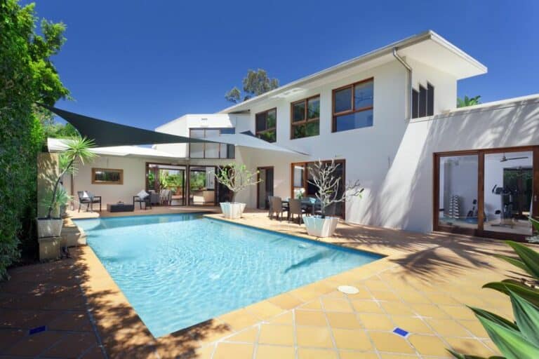 Maison moderne à deux étages avec piscine, terrasse et coin salon extérieur, doté de grandes fenêtres et d'espaces ombragés.
