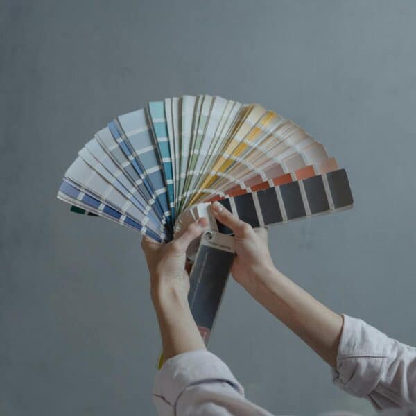 Mains tenant un livret d'échantillons de couleurs de peinture en éventail sur un fond gris.