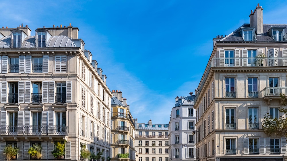 Immeubles parisiens traditionnels aux façades crème, aux toits mansardés gris et aux nombreuses fenêtres sous un ciel bleu limpide.